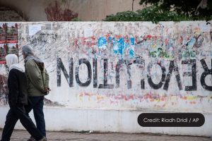 Image of two men walking past a wall that has revolution