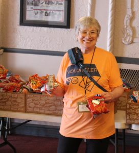 World Cinema Day volunteer with short hair, wearing an orange shirt and holding out snacks to give away inside the Barrymore Theater. 