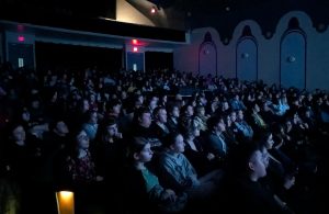 Crowd of school age youth watching a the screen inside a movie theater. 